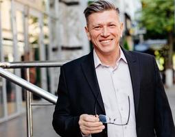 Happy senior businessman holding glasses in his hand in city outdoor.- Image photo