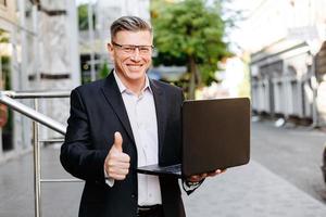 Feliz empresario sosteniendo portátil abierto, sonriendo con el pulgar hacia arriba- imagen foto