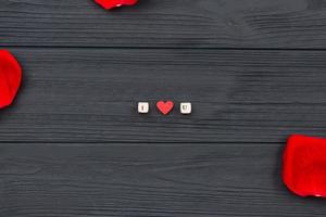 On a wooden background, the phrase I love you with cubes with letters and red rose petals. photo