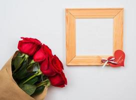 Red, beautiful roses and wooden frame lie on a white background photo