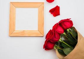 On a white background there are beautiful red roses and a frame. Place for text, copy space photo