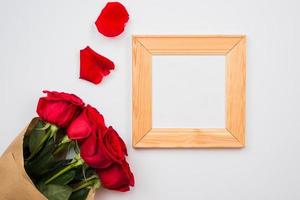 On a white background there are beautiful red roses and a frame. Place for text, copy space photo