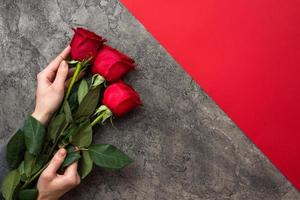 Hand holding bouquet of red roses isolate on grey with red background photo