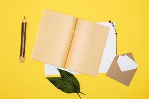 envelope with white sheets, open notebook and pencil  lie  on a yellow background photo