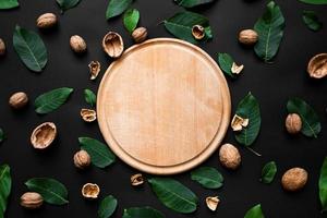 nutshell and fresh green leafs  scattered on a black background. Wooden cutting board in the centre photo