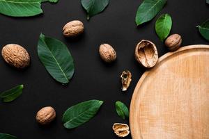 Closeup nutshell and fresh green leafs  on a black background. Part of wooden cutting board photo