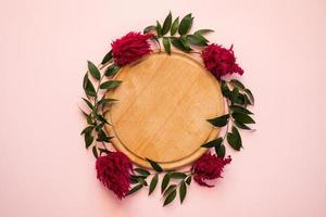Arch of fresh flowers lie on a pink background - Wooden cutting board in the center. Copy space photo