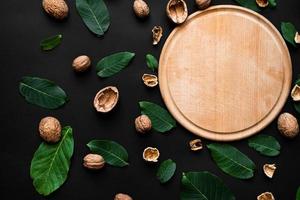 nutshell and fresh green leafs  scattered on a black background. Wooden cutting board on the rigth side photo