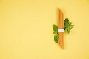 Spaghetti, basil on a yellow background. Top view. Copy space for text. photo