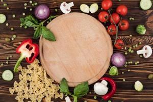 Italian products near round wooden board surrounded by cherry tomatoes and garnished with greens, pasta, peper photo