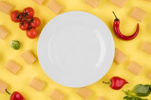 Empty plate on yellow background with pasta, tomatoes, pepper. photo