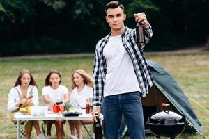 Hombre de pie sosteniendo una cerveza y mirando a la cámara al aire libre en el camping foto