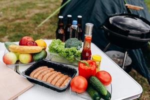 cerveza, salchichas y verduras frescas en la mesa al aire libre. - acampar foto