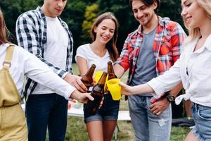 Primer plano de la imagen de una empresa de amigos levantando botellas con una cerveza en el camping foto