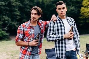 Two guys standing and holding a beer  in the camping. - Image photo