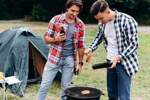Two guys cooking a sausages on the barbecue in the camping. - Image photo