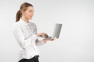 Sonriente mujer de negocios en camisa blanca sosteniendo un portátil y trabajando mientras está de pie foto