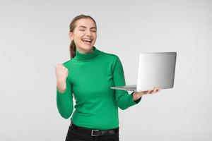 Happy girl looking at laptop with laughing surprised expression . Holds device and fist up. - Concept image photo