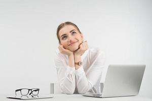 Dreamy  business woman sits next a laptop and looks up puting her head on the  her arms photo