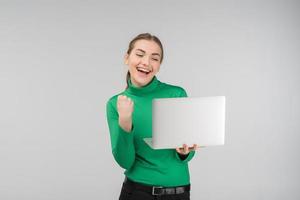 Enthusiastic young woman looking at laptop with victorious expression . Holds device and fist up. - Concept image photo