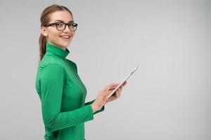 Chica de perfil alegre sosteniendo una tableta en sus manos y sonriendo foto