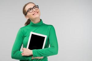 Smiling dreamy girl hugging her ipad and looking up photo