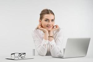 Smiling pretty woman sitting next a laptop and looking at the camera puting her head on the  her arms photo