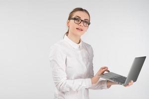 Business woman in glasses  works on a laptop while standing. Looking at the camera photo