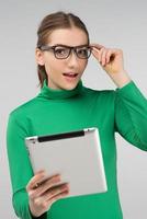 young girl with glasses holding a tablet in her hands and very surprised photo