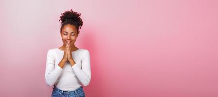 Portrait of woman in supplication pose with smile and close eyes over pink background. Copyspace photo