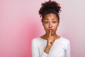 Cute woman shows a silence gesture touching by index finger her lips. Concept gesture - Image