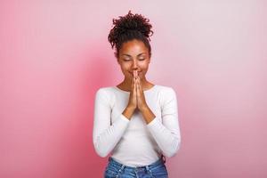 Studio portrait of woman in supplication pose with smile and close eyes over pink background photo