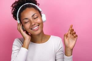 Portrait of a delightful girl with closed eyes in earphones listening to music over pink background photo