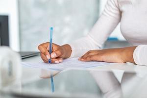 Primer plano de manos femeninas durante la escritura con lápiz sobre un papel, mujer de negocios firmando un documento foto