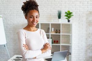 Charming woman in office, folded arms and smiling looking at the camera leaned the table photo