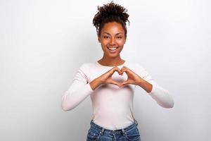 Cute mulatto woman shows a heart gesture with her fingers next her chest. Concept gesture - Image