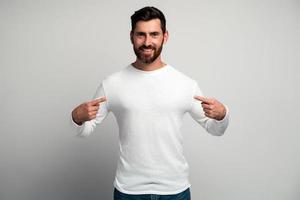 Portrait of conceited man in white shirt pointing at himself and looking with arrogant selfish expression, feeling successful and self-important. Indoor studio shot isolated on white background photo