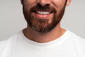 Close up retrato de feliz guapo empresario barbudo de pie y sonriendo. Foto de estudio en interiores, aislado sobre fondo gris claro