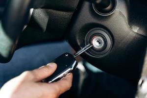 El enfoque selectivo de la mano masculina da cuerda a la llave de encendido del automóvil, la conducción del automóvil y el tablero de instrumentos. concepto de viaje y transporte foto