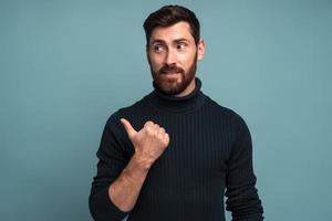 Portrait of happy excited man with beard pointing side with his finger, find out solution or idea, get answer on question, eureka. Indoor studio shot isolated on blue background photo