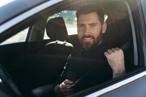 feliz hombre caucásico sentado y mirando por la ventana mientras tiene un largo camino por el coche. gente ocupada y concepto de transporte foto