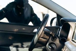 Vista desde el coche al hombre vestido de negro con un pasamontañas en la cabeza mirando el cristal del coche antes del robo. ladrón de autos, concepto de robo de autos foto