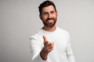 Hombre barbudo extremadamente feliz riendo y señalando con el dedo mirando a la cámara, broma divertida y ridícula. Foto de estudio de interior aislado sobre fondo blanco.