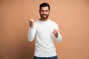 Portrait of ecstatic brunette man with beard showing yes i did it gesture and rejoicing copy space for ad. Indoor studio shot isolated on beige background photo