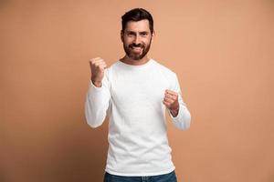 Retrato de hombre morena extasiado con barba mostrando sí lo hice gesto y regocijándose espacio de copia para el anuncio. Foto de estudio de interior aislado sobre fondo beige