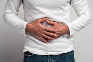 Close up view of the man holding hands on stomach feeling acute pain, suffering indigestion and nausea, duodenal ulcer. Indoor studio shot isolated on white background photo