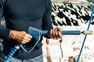 Close up view of the handsome young man holding high pressure gun while preparing to spraying at his car during the cleaning. Stock photo