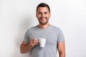 Handsome man stands holding a cup of morning tea or coffee and smilimg looking at the camera.- Image photo