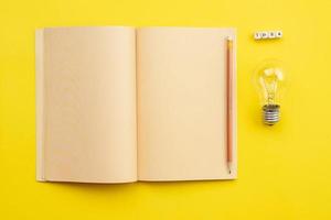 Open empty diary with a pencil and a bulb  and an  inscription idea on yellow background photo