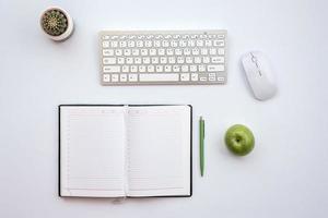 Top view office white  desk with a mouse and keyboard. Next a fresh apple and cactus photo